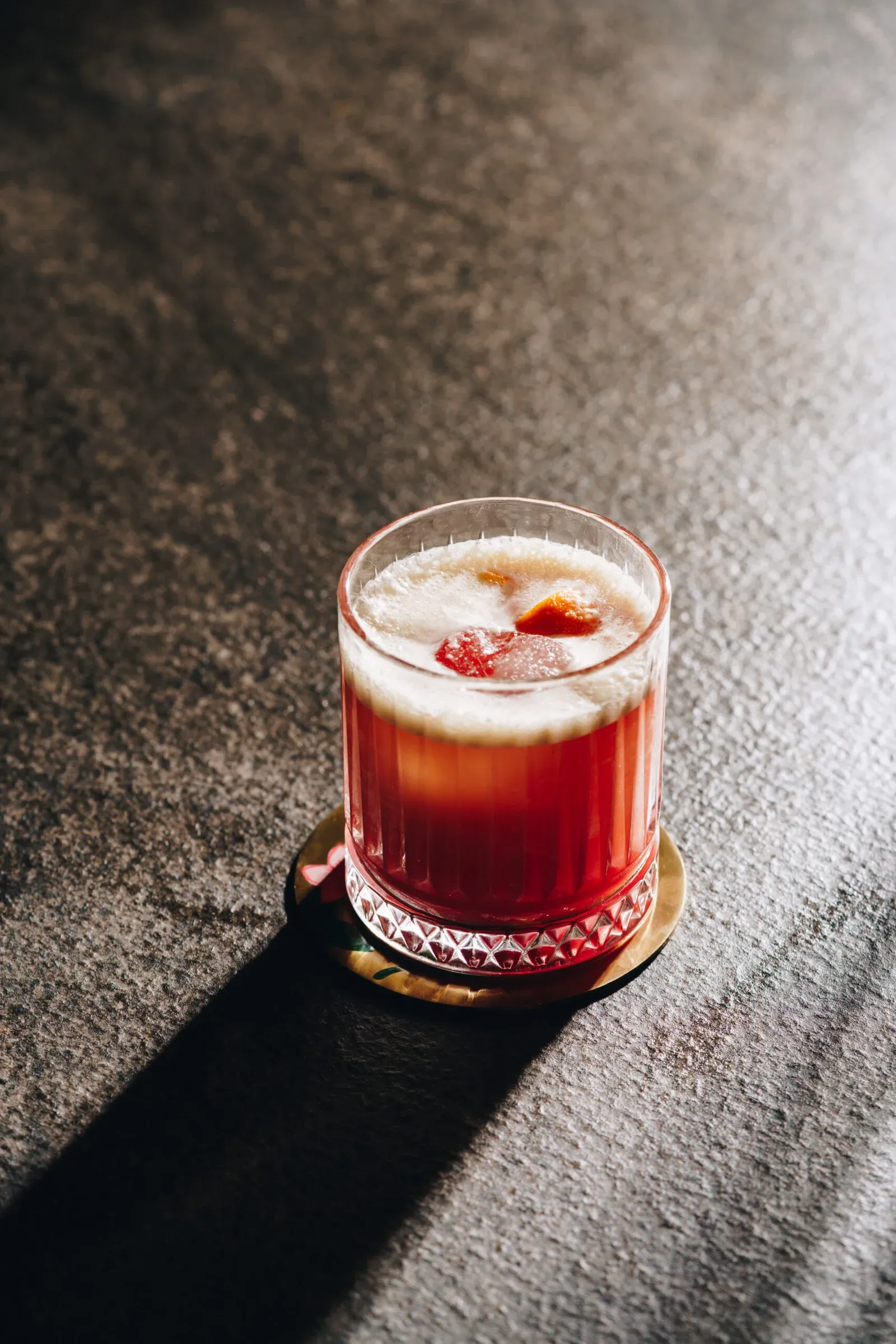 Purple Basil Red cocktail with white foam in a faceted glass